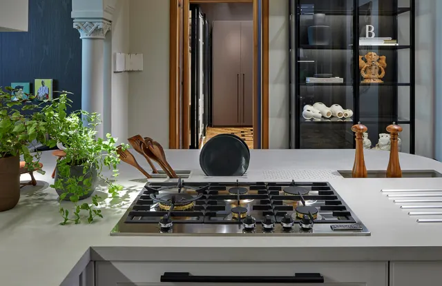 Cooktop a gás de seis queimadores em uma ilha clara, com ervas, utensílios de madeira e estante de vidro ao fundo